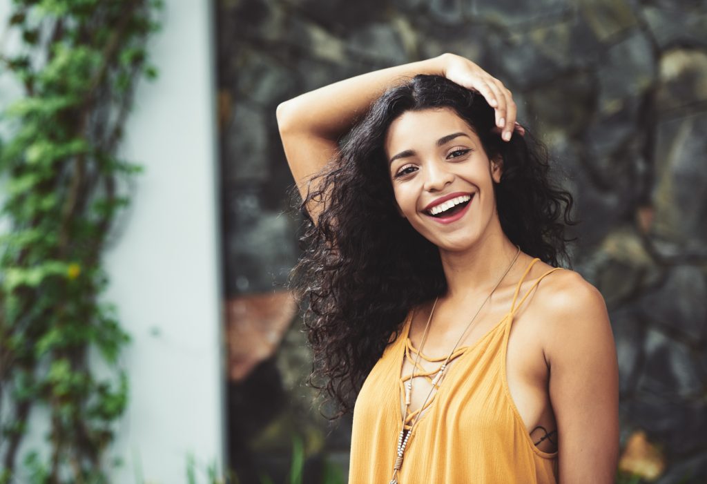 A happy young woman holding her hair after implementing the Curly Girl Method 