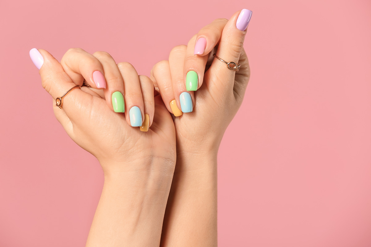 A person’s hands with colorfully painted nails in front of a pink backdrop in El Paso.